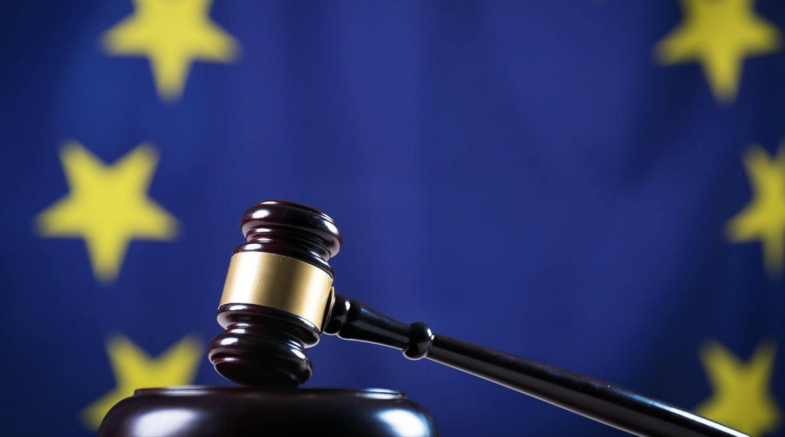 Gavel laying on a desk with the European Union flag hanging in the background.