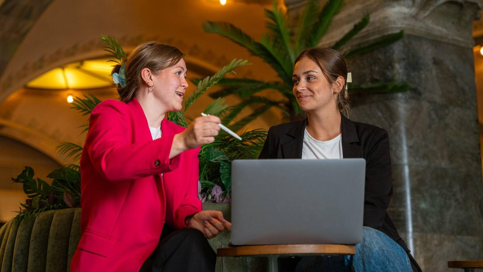 One Cemasys employee in a red blazer explaining something to another employee while sitting down.