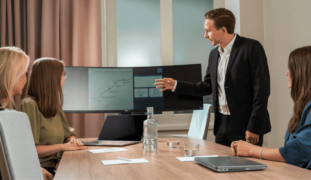 Three Cemasys employees sitting around a conference table, while another is presenting a report on a screen.